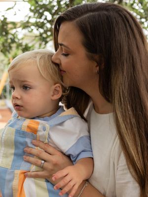 A loving mother gently kisses her young blonde toddler on the cheek while holding him close outdoors.
