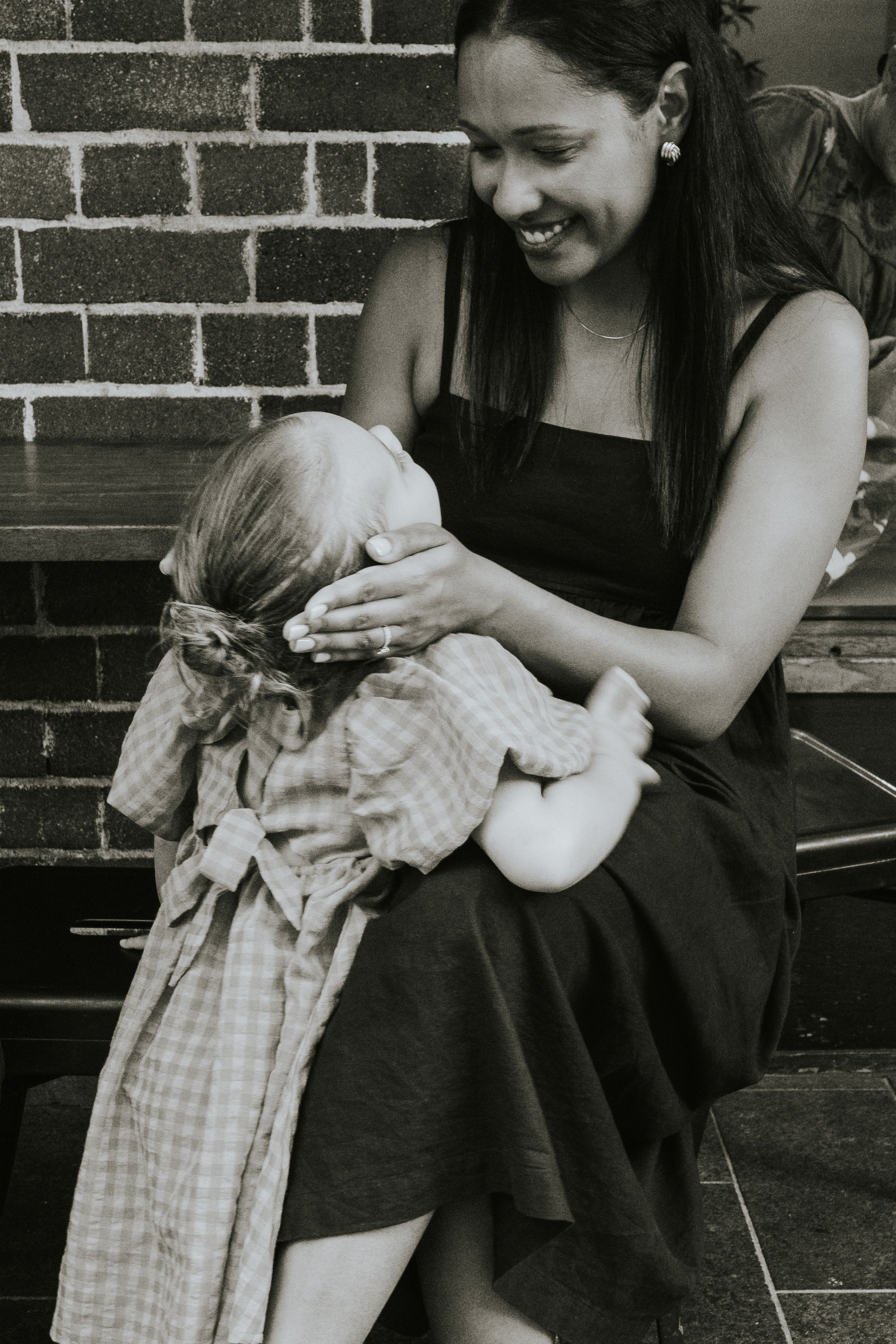 Black and white photo of smiling mother breastfeeding infant on outdoor steps.