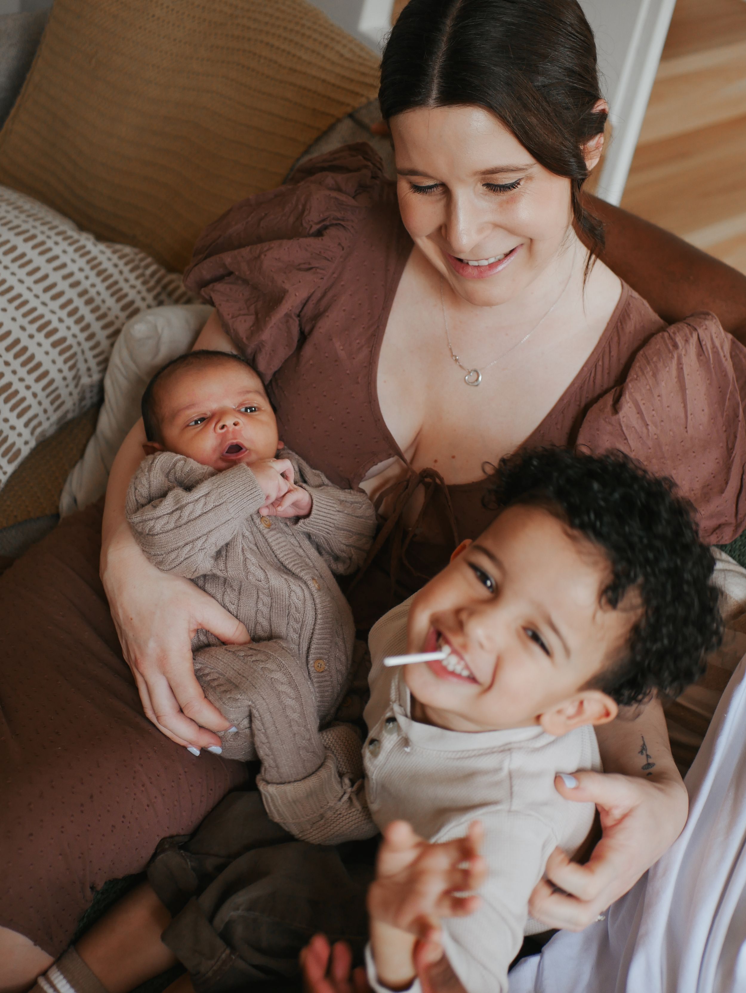 Smiling brunette mother holding newborn baby with happy toddler son beside her.