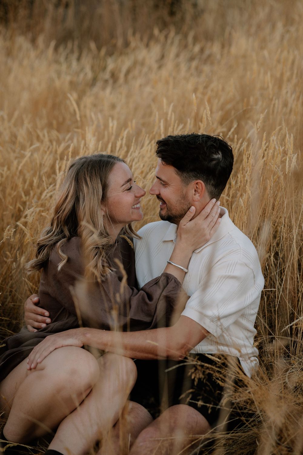 A romantic couple embraces in a sunlit field of tall grass during a golden hour photoshoot.