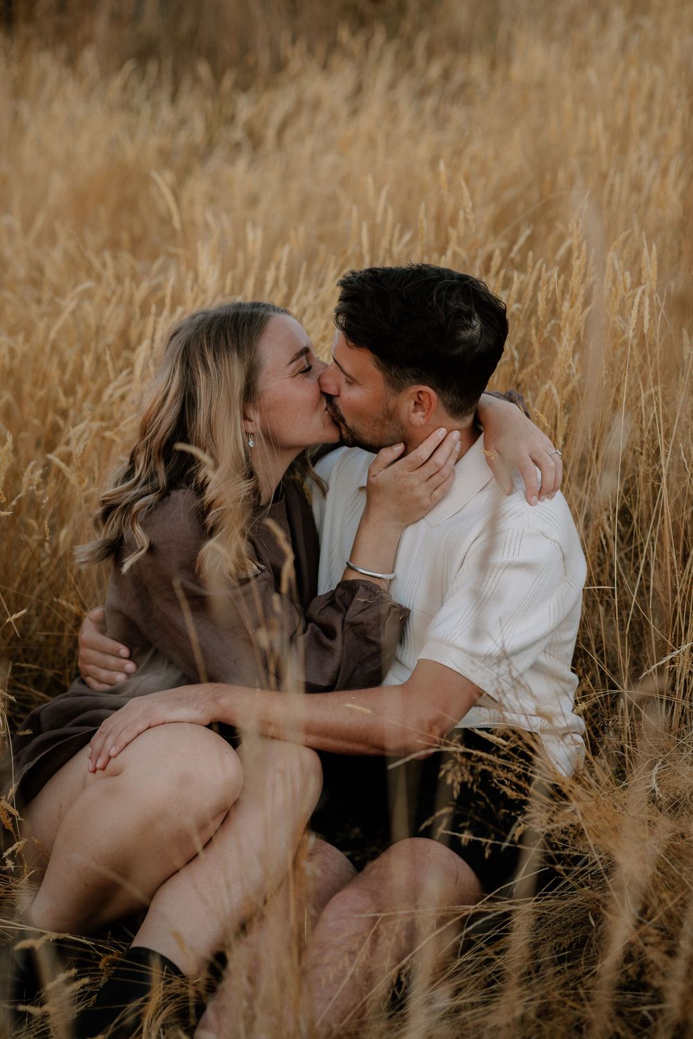 Intimate couple sharing tender moments while sitting together in a golden wheat field.