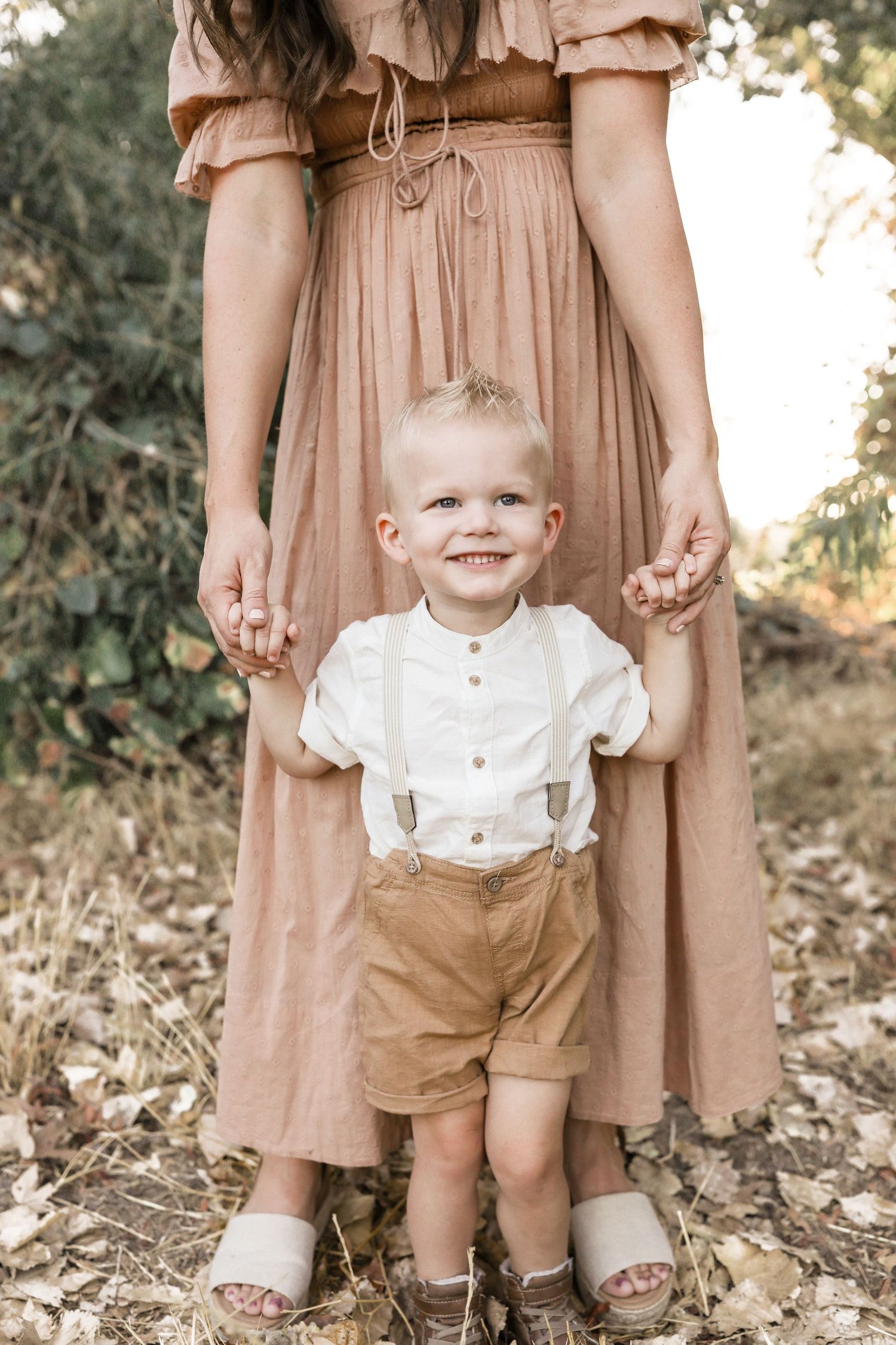 Smiling man in white t-shirt carries happy toddler on his shoulders outdoors on a dirt path.