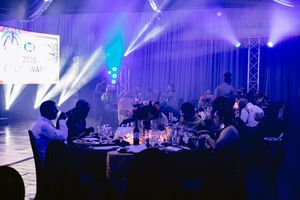 Elegant gala dinner event with round tables, dramatic blue and purple lighting, and guests in formal attire.