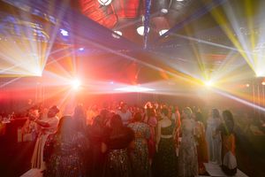 Crowd of elegantly dressed guests dancing under colorful laser lights at a glamorous indoor event.