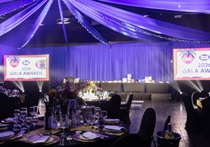 Elegant gala awards banquet hall with purple lighting, draped ceilings, set tables, and illuminated award ceremony signs.