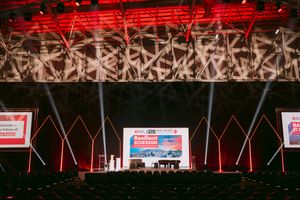 Large conference stage with red lighting and screens at a professional event in an auditorium.