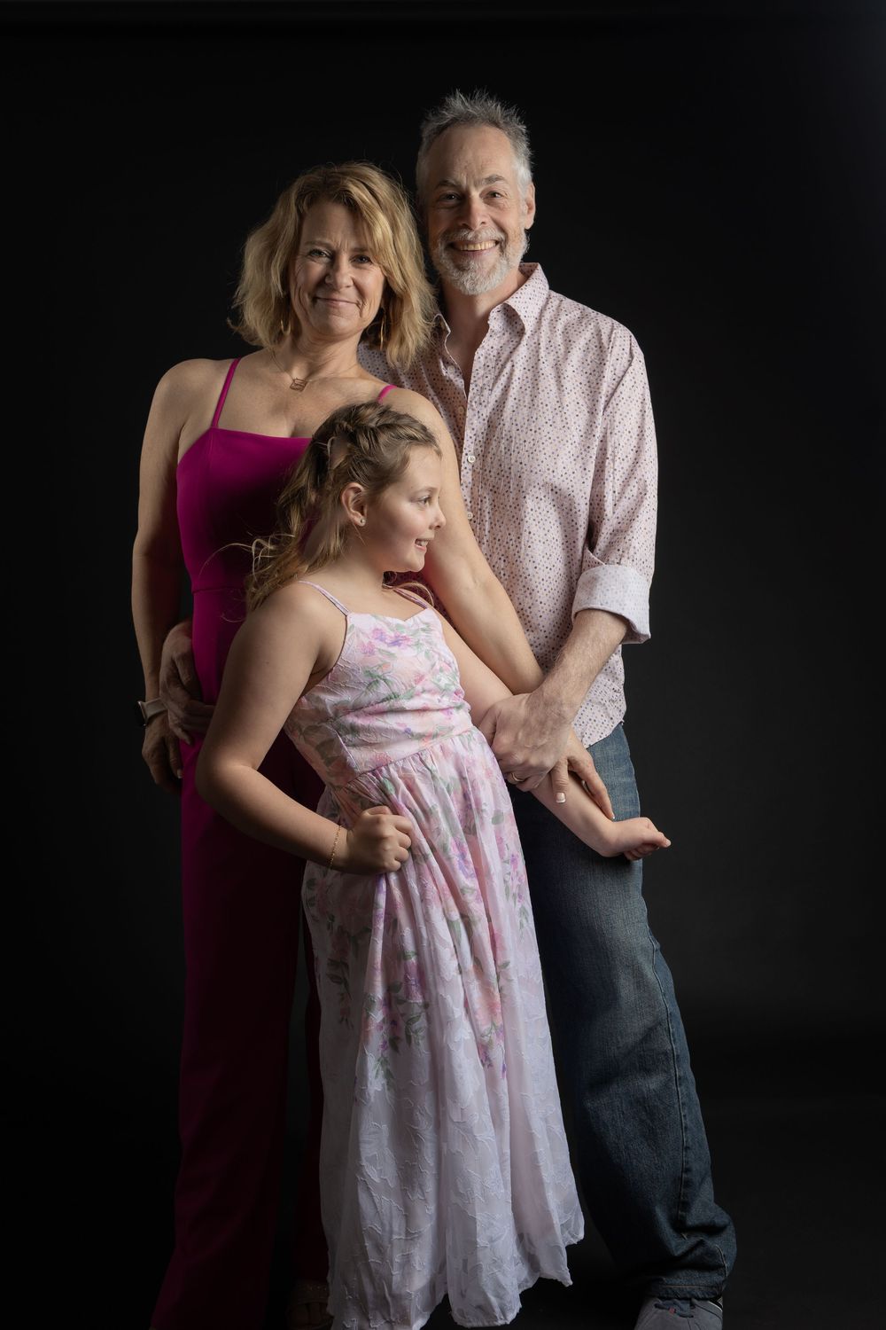 Family portrait of two adults and a young girl in formal attire posing together against a dark background.