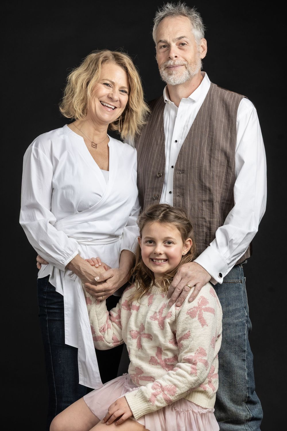 A smiling family of three poses together in a professional studio portrait.