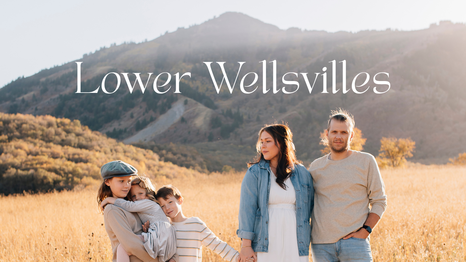Family posing in golden field with mountain backdrop, text overlay reads Lower Wellsvilles.