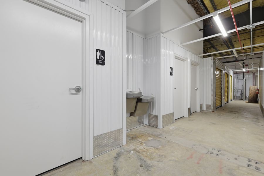 Clean white restroom corridor in a storage facility with ADA-accessible bathroom doors and concrete floors.