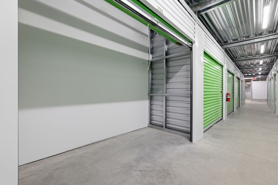 Modern self-storage facility hallway with bright green roll-up doors and polished concrete floors.