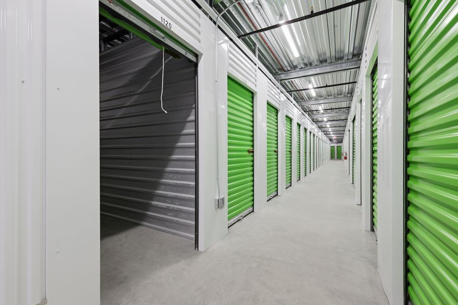 Bright hallway of self-storage units with green roll-up doors and gray doors on the left side.