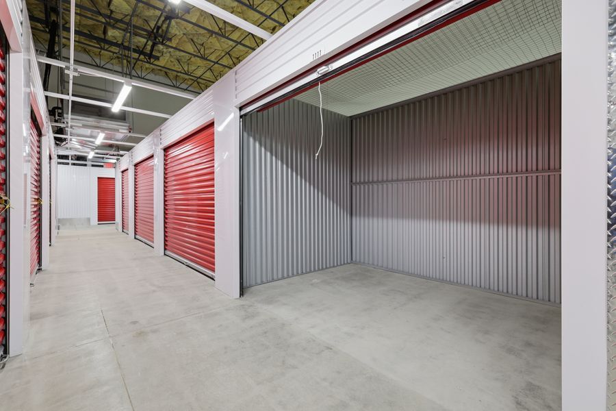 Interior view of a clean self-storage facility with open red roll-up doors lining a wide concrete corridor.