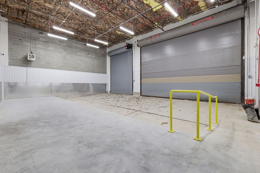 Spacious warehouse interior with concrete floors, two large roll-up doors, and yellow safety barriers.