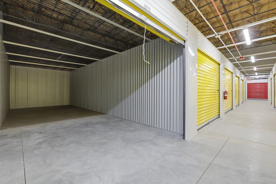 Indoor self-storage facility hallway with open unit, yellow roll-up doors, and concrete floors.