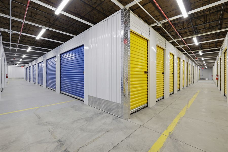 Indoor self-storage facility with blue and yellow roll-up doors under bright fluorescent lighting.