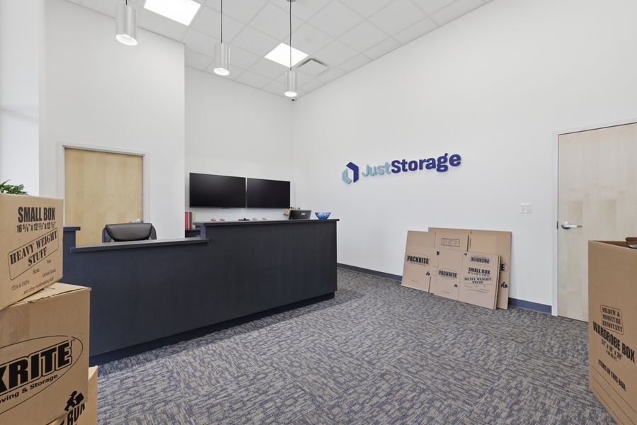 Just Storage facility front office with reception desk, monitors, moving boxes, and branded signage.