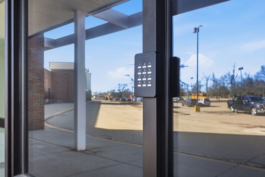Glass door entrance with keypad access control panel overlooking a parking lot.