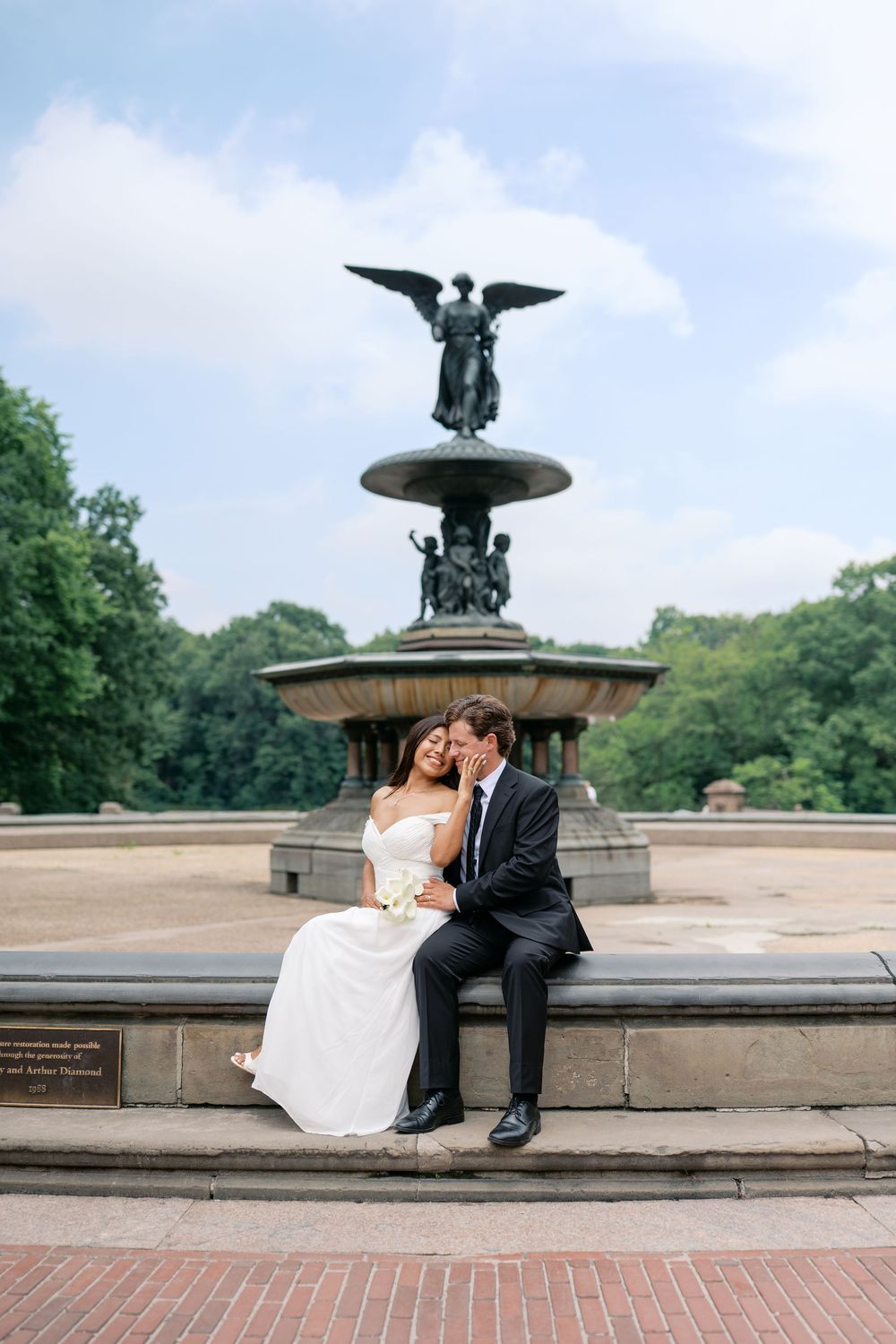 Bride and groom sitting together at Bethesda Fountain in Central Park, NYC, on their wedding day.