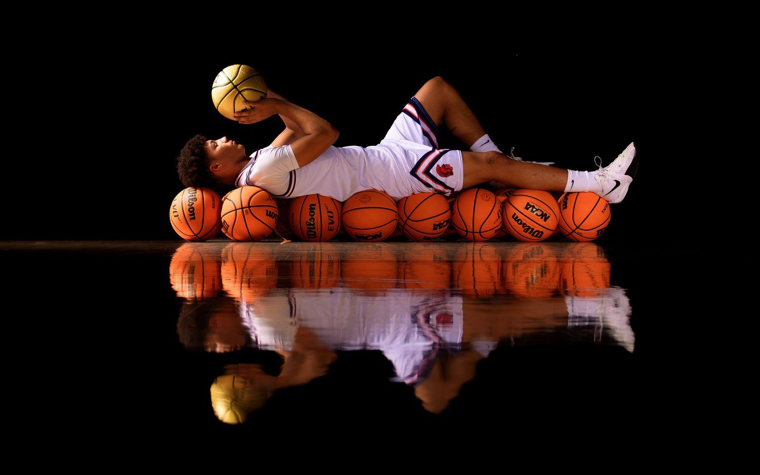 Hershey boys basketball senior lying on basketballs, reflection media day portrait, by Deanna Fox, SportsFox Photography based in Hershey PA