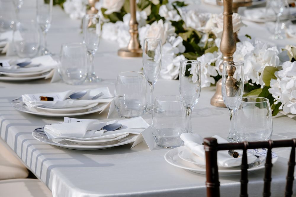 Elegant white wedding reception table setting with crystal glassware, white plates, and golden candlesticks.