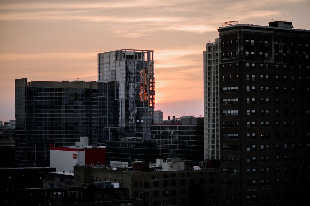 City skyline at sunset with modern skyscrapers silhouetted against a warm orange and purple sky.
