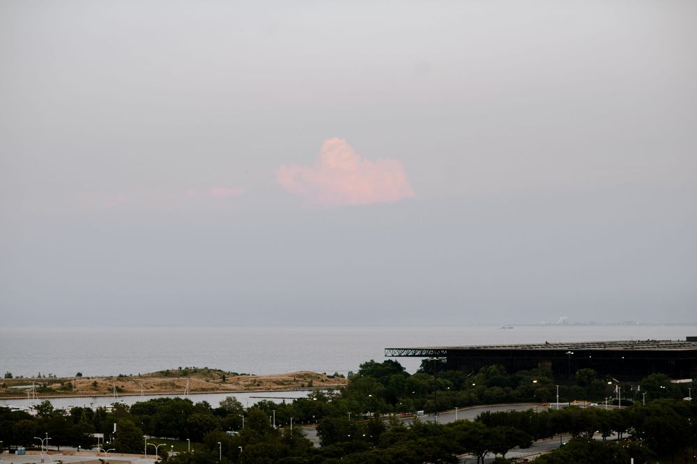 Pink cloud formation over calm ocean waters with a waterfront structure visible at dusk.
