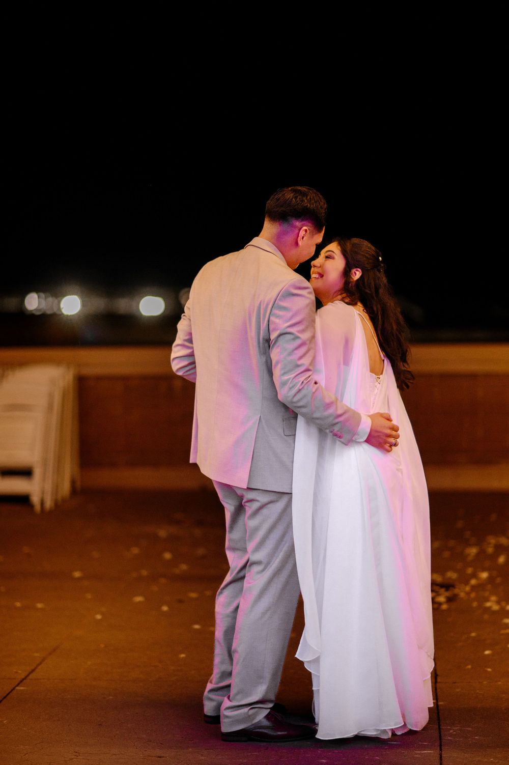 Bride and groom share romantic first dance outdoors at night under soft pink lighting.