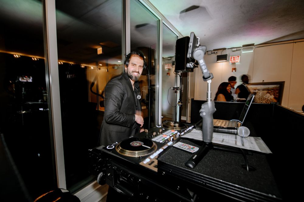 DJ smiling at turntables during a wedding reception in a dimly lit modern venue.