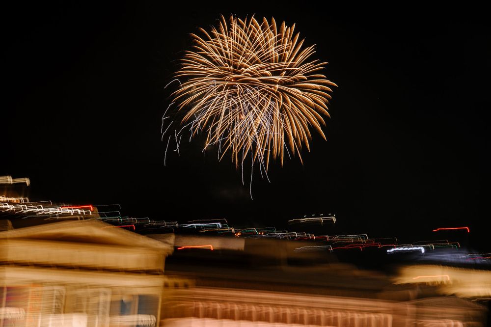 Golden fireworks burst over blurred city buildings at night during outdoor wedding celebration.