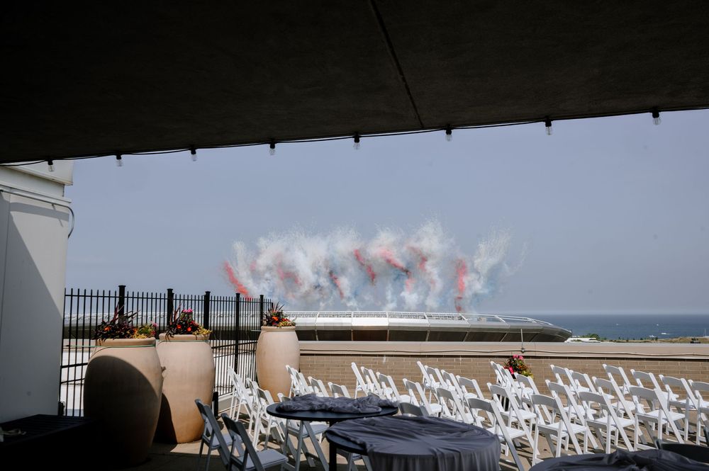 Rooftop wedding venue with white chairs and colorful smoke display over the ocean in background.