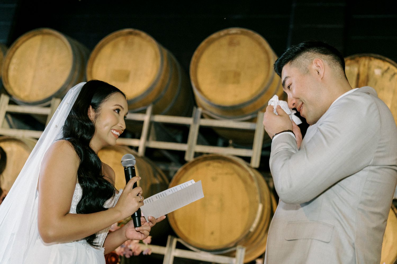 Bride reads wedding vows while emotional groom wipes tears in a winery ceremony surrounded by oak barrels in the bethnal. Newstead Brisbane