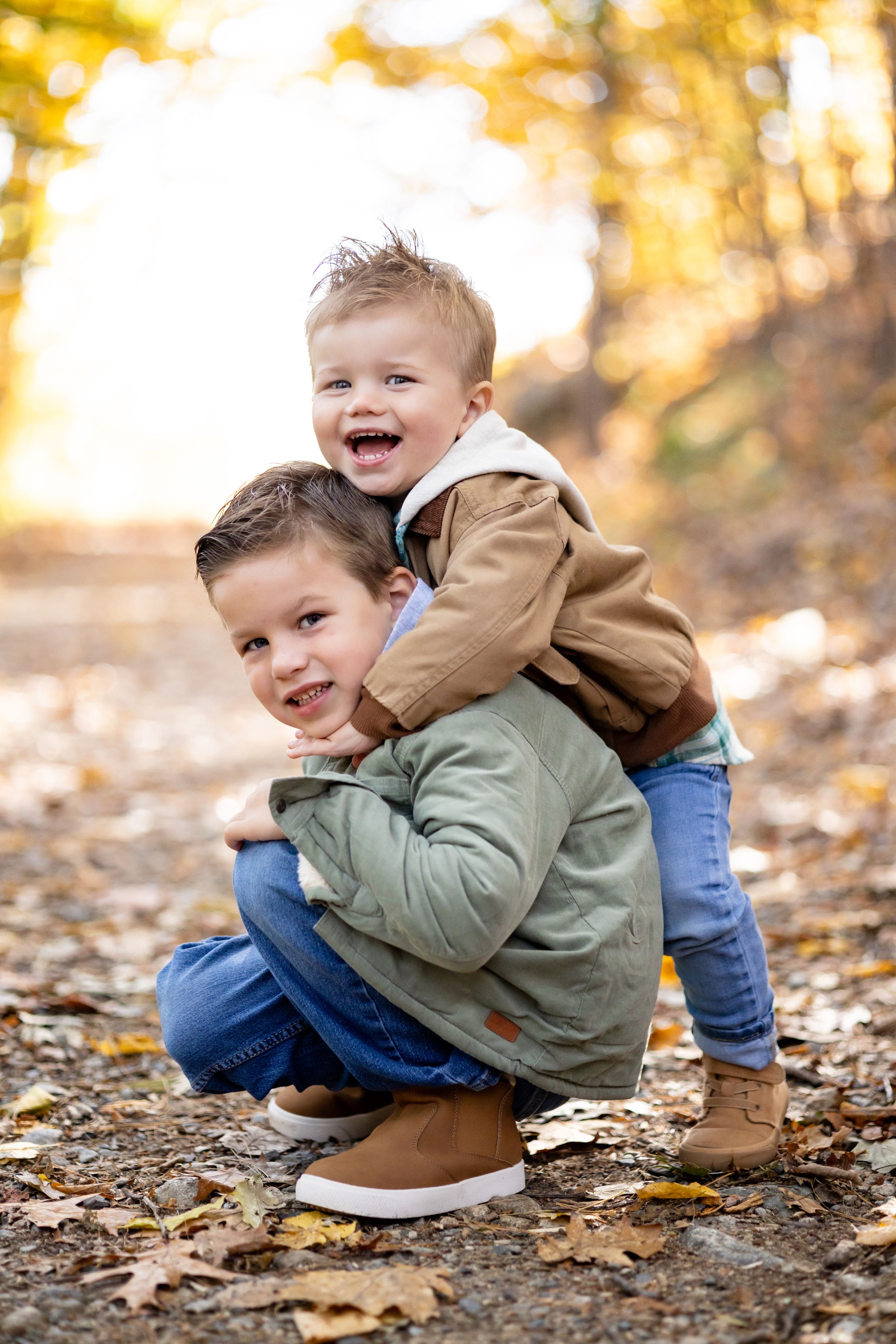 Two young boys playing outdoors in autumn, one giving the other a piggyback ride among fallen leaves.