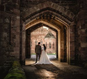 Bride and groom silhouetted in a stunning stone archway at a historic castle wedding venue.