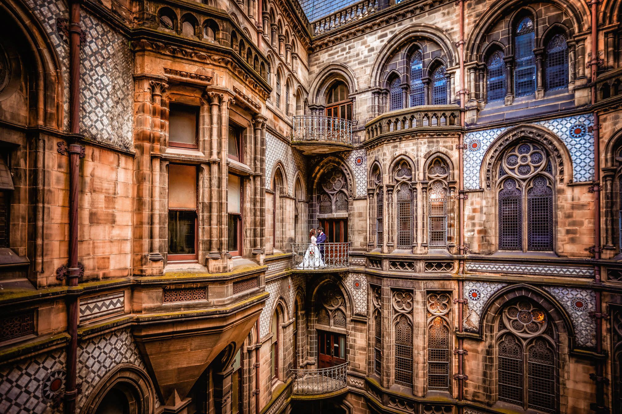 Gothic courtyard with ornate arches, colorful tiles, and a bride in white standing on a balcony.