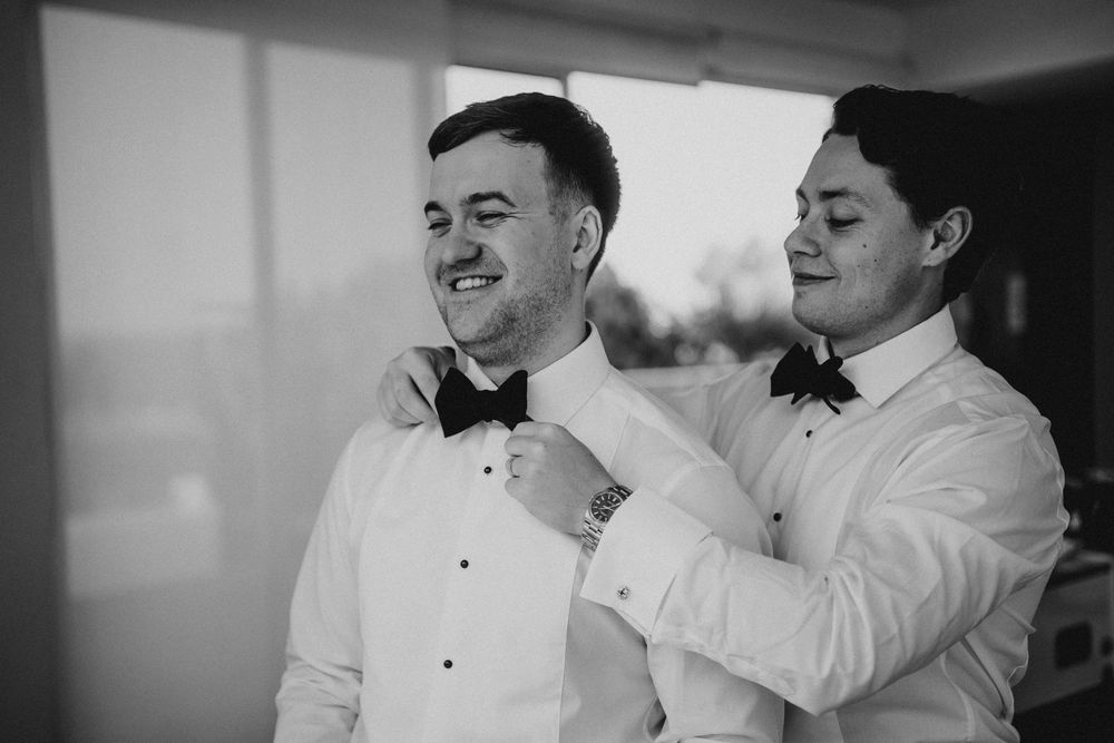 Black and white photo sequence showing two people in formal white attire helping each other adjust their bowties.