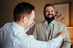 Two men share a joyful moment together, with one wearing a beige suit and tie while the other is in a white shirt.
