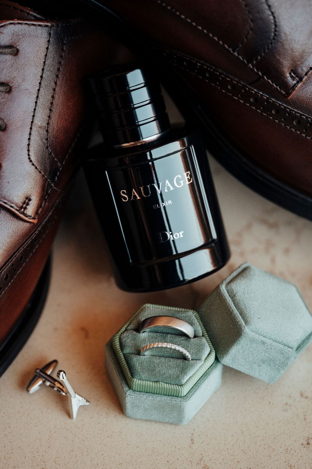 A luxury perfume bottle of Dior Sauvage sits elegantly beside brown leather accessories and a sage green ring box.