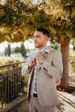 A person in a beige suit stands in dappled sunlight under autumn trees, creating a warm and elegant outdoor portrait.