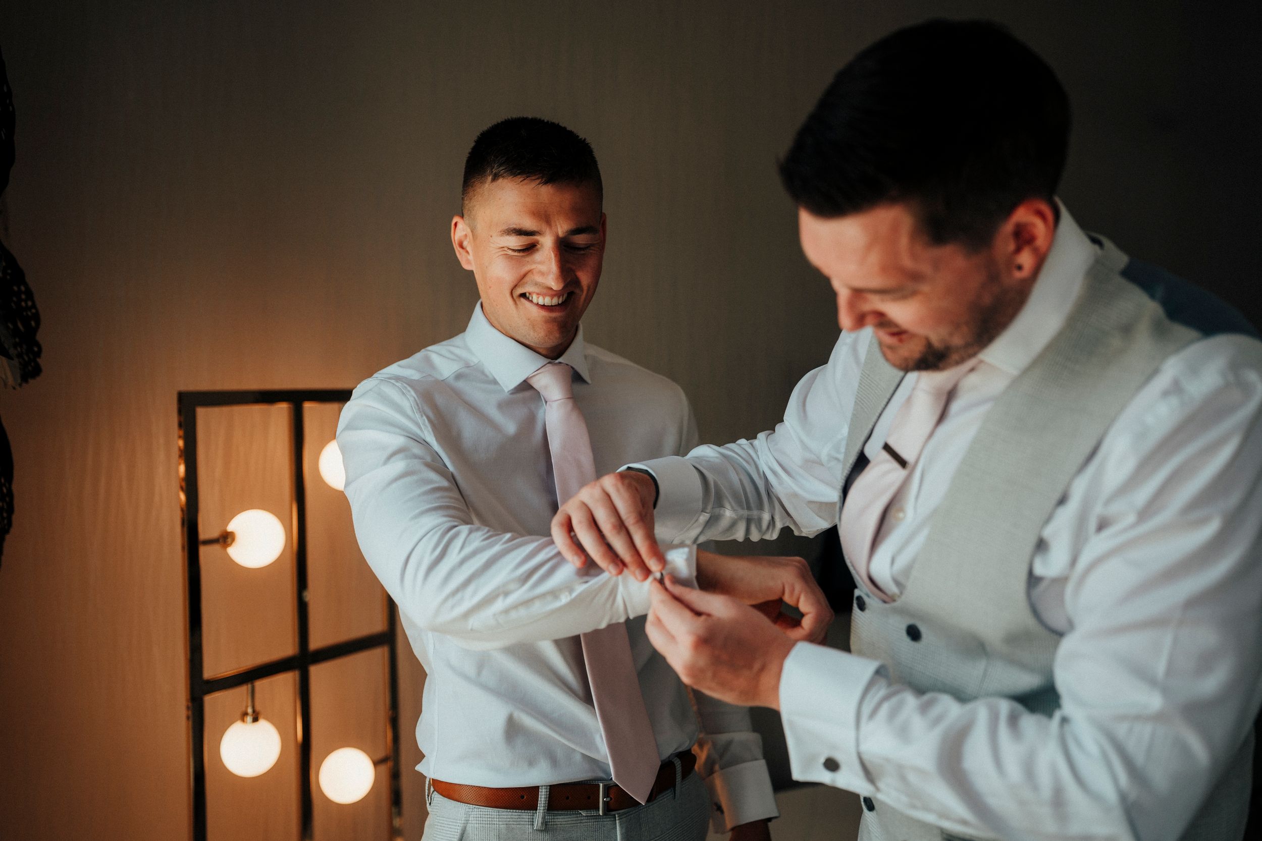 Two people in white dress shirts embrace and dance together in a dimly lit room with pendant lights.