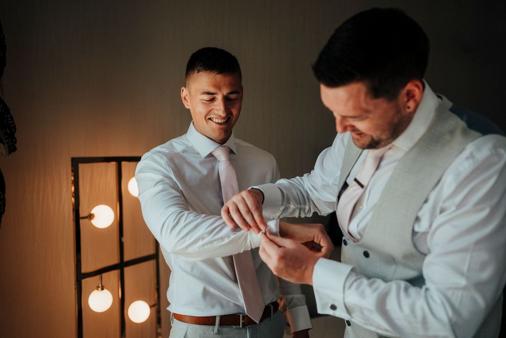 Two people in white dress shirts embrace and dance together in a dimly lit room with pendant lights.