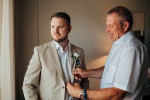 A tender moment between two men as one helps adjust the other's boutonniere on a wedding day.