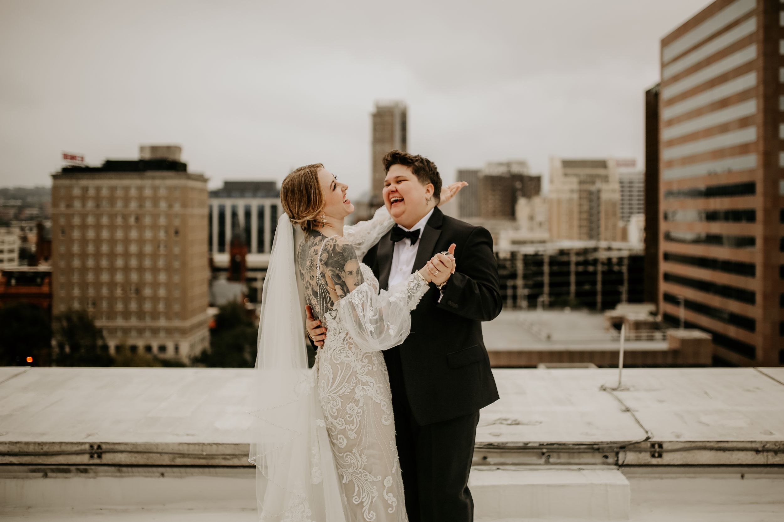 Newlyweds share a romantic dance on a rooftop with city skyline in the background.