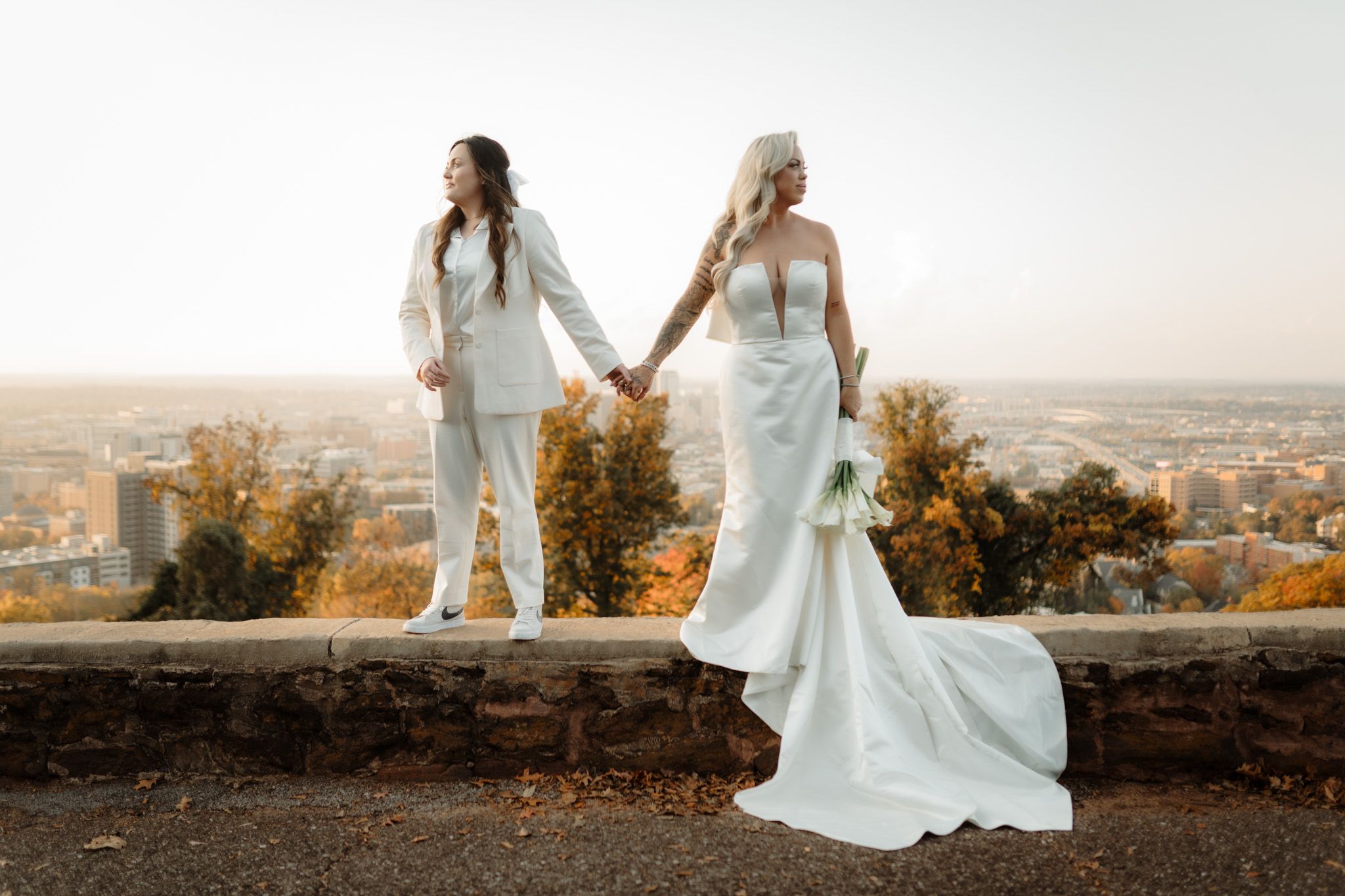 Two people in white dresses pose against cityscape backdrop during golden hour.