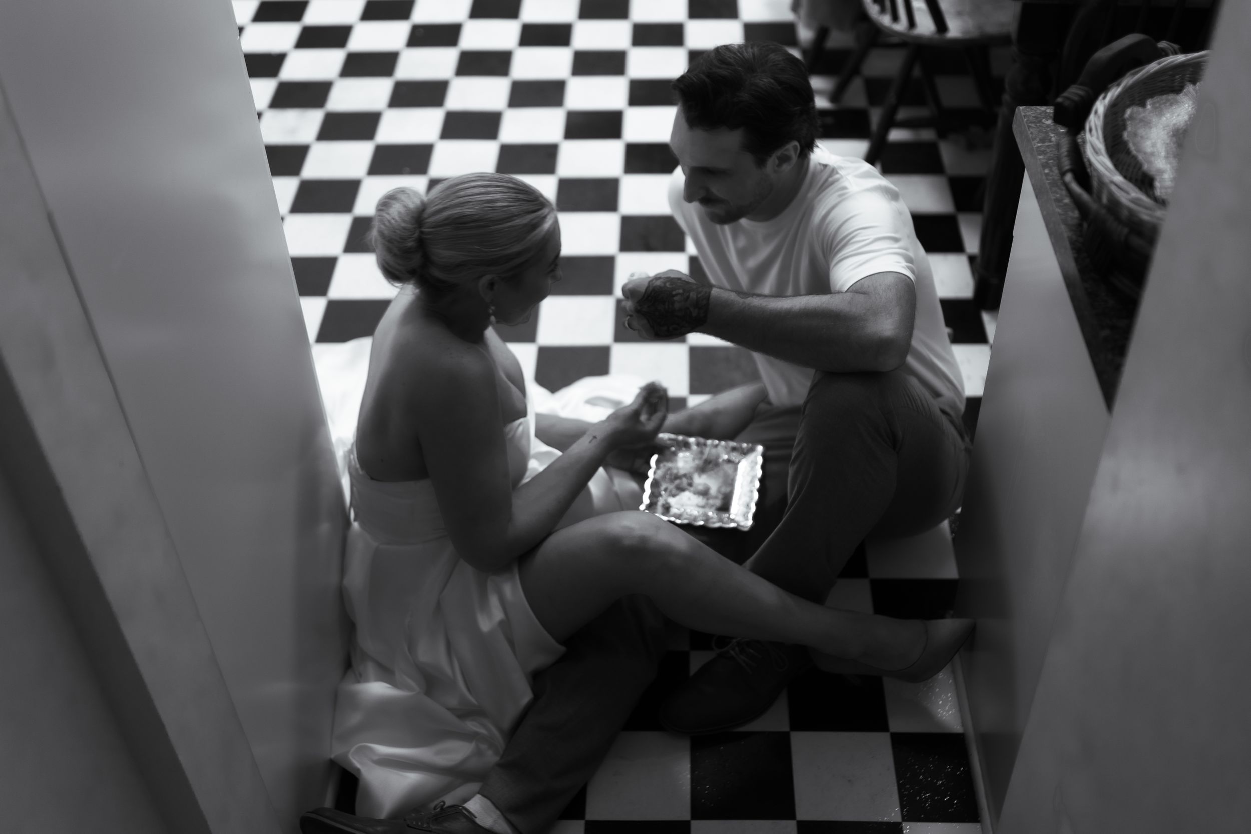 Black and white image of two people sitting on a checkered floor looking at something together.