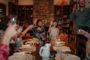 Group of friends raising glasses in a toast around a festive dinner table in a cozy stone-walled dining room.