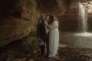 A romantic moment captured under a rocky overhang with a waterfall in the background.