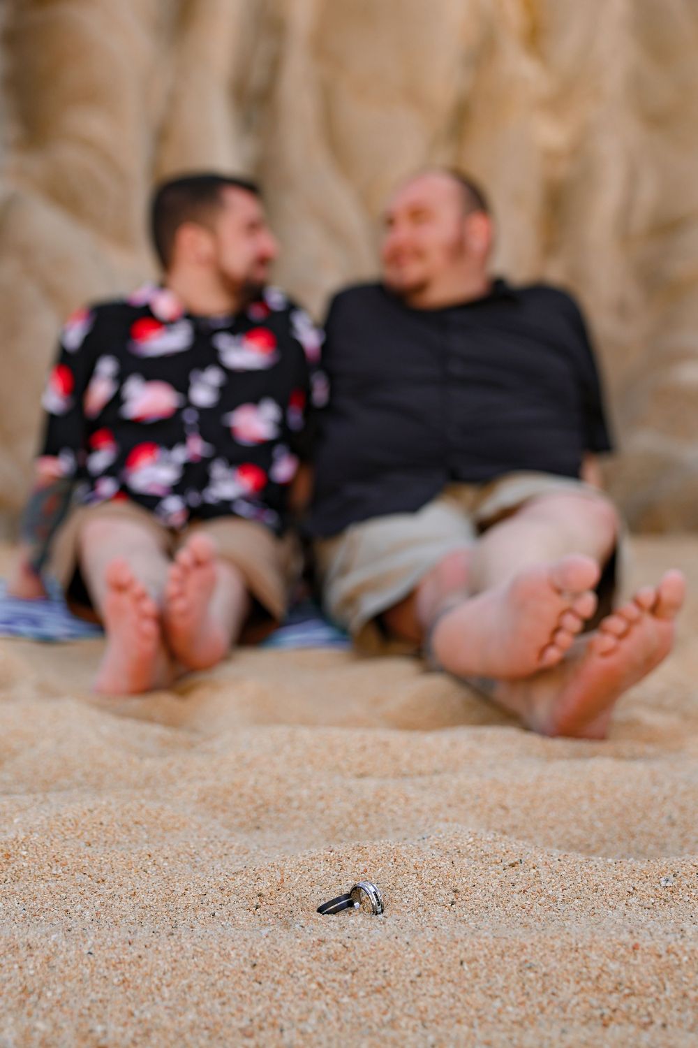 Two people relaxing on beach sand with a small object in foreground.
