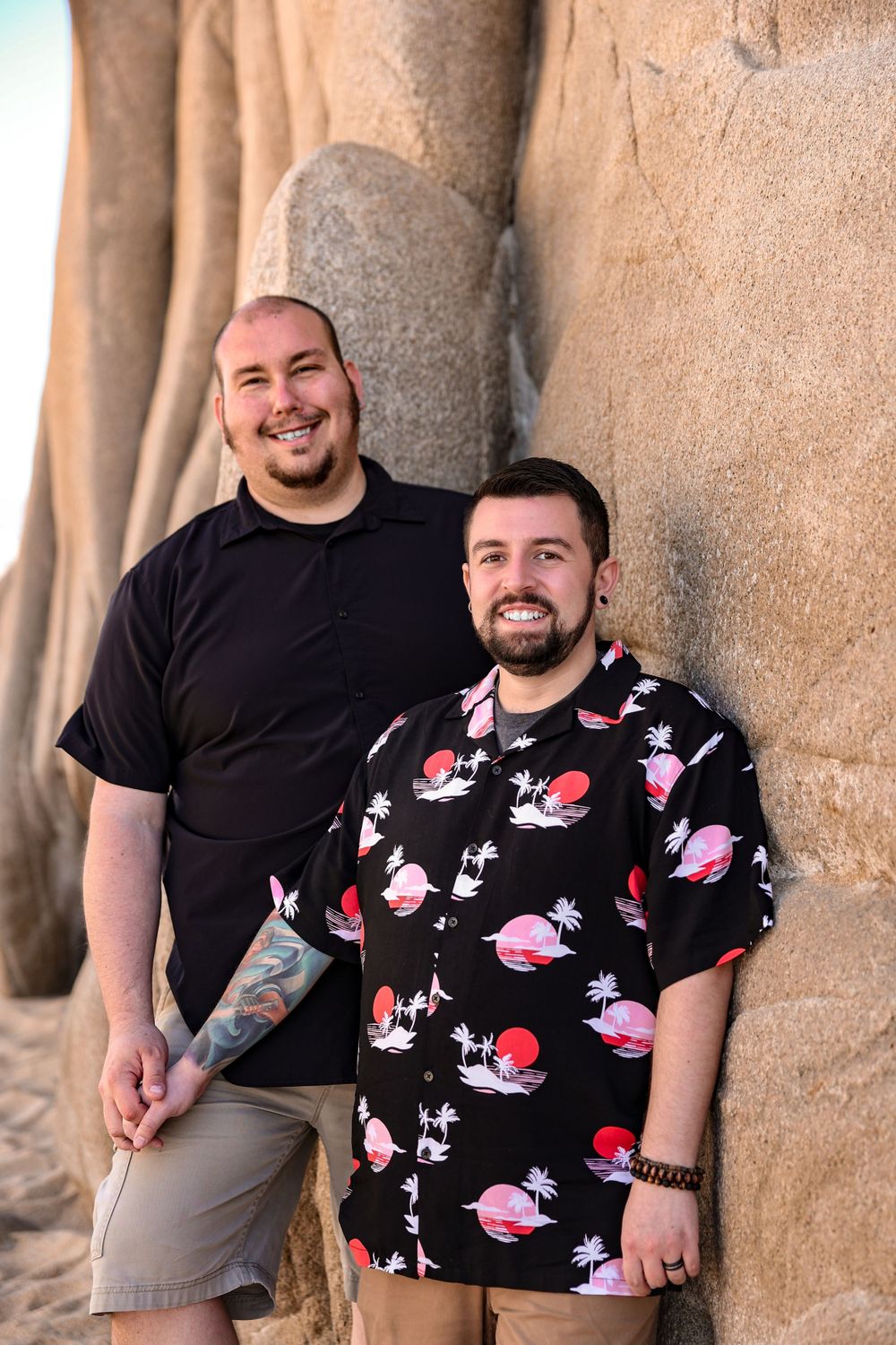 Two people posing against textured rock formation wearing contrasting casual outfits.
