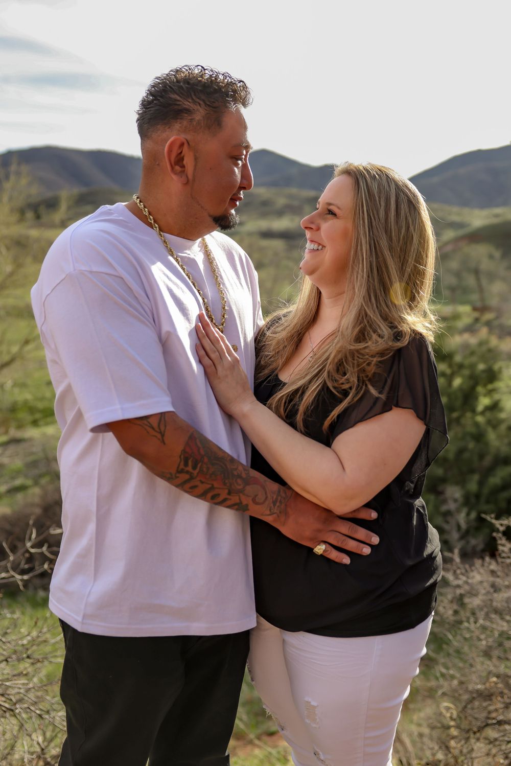 A couple embraces in front of scenic mountain landscape during golden hour photography session.